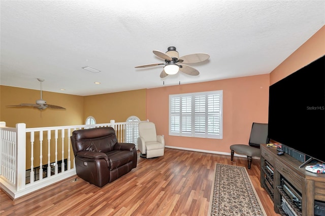 living area with a textured ceiling, wood-type flooring, and ceiling fan