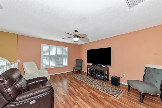 living room featuring a textured ceiling, wood-type flooring, and ceiling fan