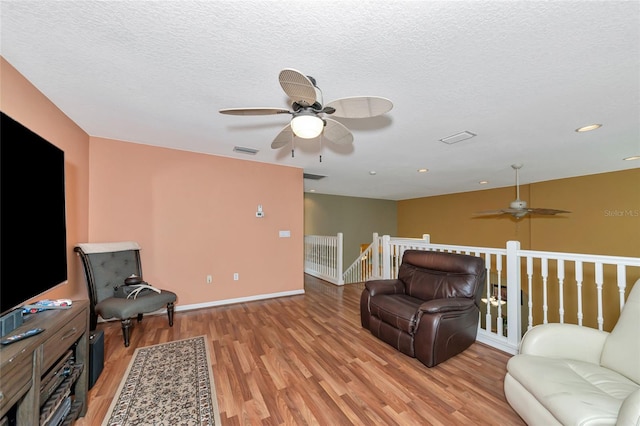 living room featuring a textured ceiling, ceiling fan, and light hardwood / wood-style flooring