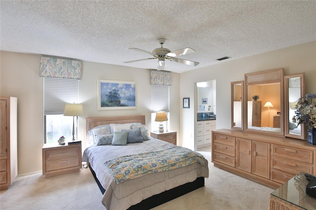 bedroom with a textured ceiling, ensuite bath, light carpet, and ceiling fan