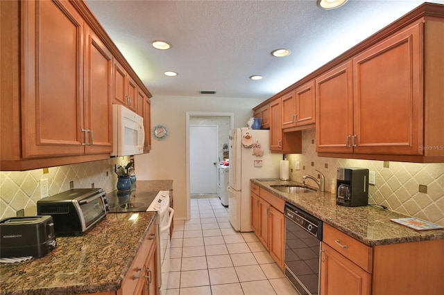 kitchen with separate washer and dryer, dark stone counters, light tile patterned floors, sink, and white appliances