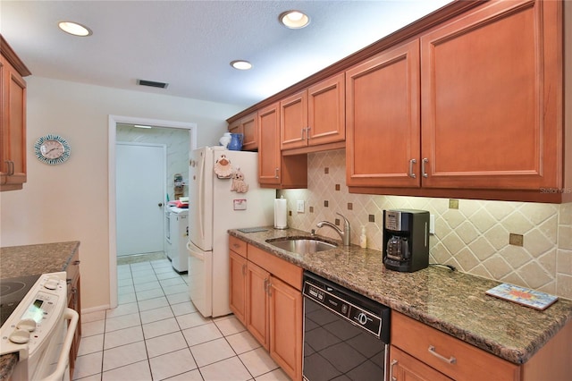 kitchen featuring sink, dark stone counters, light tile patterned floors, washer and clothes dryer, and white appliances