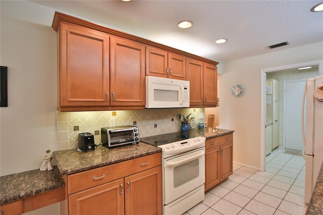 kitchen featuring tasteful backsplash, dark stone counters, white appliances, and light tile patterned flooring