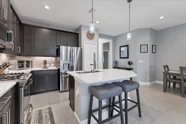 kitchen with dark brown cabinetry, backsplash, pendant lighting, a center island with sink, and appliances with stainless steel finishes