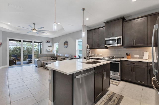 kitchen with appliances with stainless steel finishes, tasteful backsplash, dark brown cabinetry, a center island with sink, and decorative light fixtures