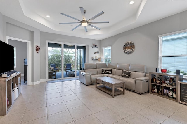 living room featuring ceiling fan, light tile patterned floors, and a tray ceiling