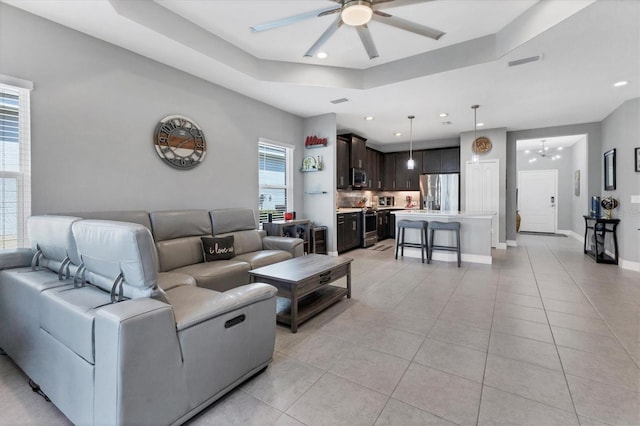 tiled living room with a tray ceiling and ceiling fan with notable chandelier