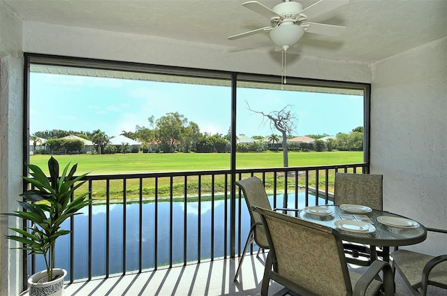 sunroom with ceiling fan and a water view