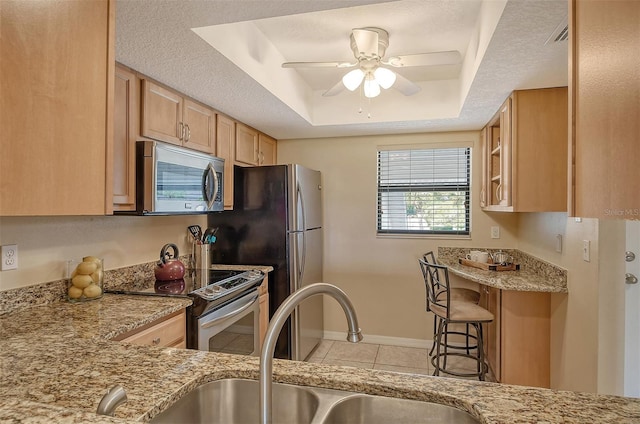 kitchen with appliances with stainless steel finishes, light tile patterned floors, sink, a breakfast bar, and a tray ceiling