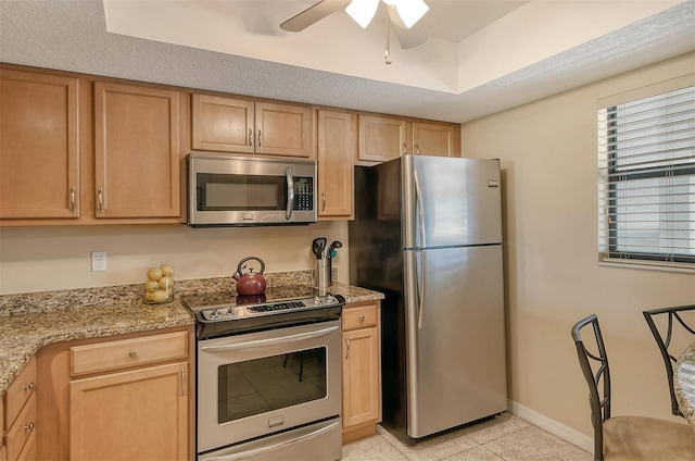 kitchen featuring appliances with stainless steel finishes, light tile patterned floors, light brown cabinets, light stone countertops, and ceiling fan