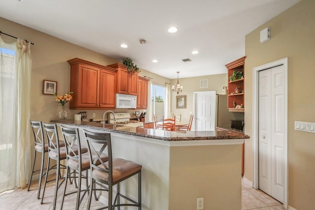 kitchen with kitchen peninsula, a breakfast bar area, dark stone counters, pendant lighting, and white appliances