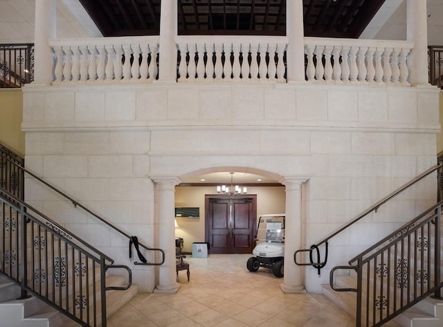 tiled entryway with a towering ceiling, crown molding, a chandelier, and decorative columns