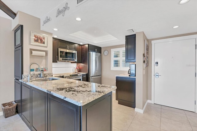 kitchen featuring appliances with stainless steel finishes, kitchen peninsula, sink, light stone counters, and a tray ceiling