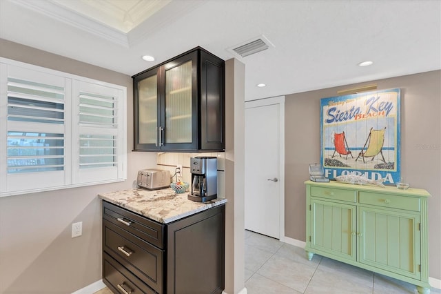 kitchen featuring light stone counters, ornamental molding, a raised ceiling, and light tile patterned floors