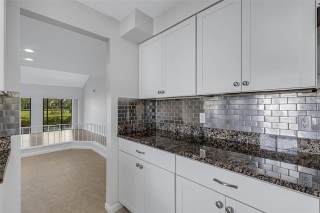 kitchen with lofted ceiling, white cabinets, tasteful backsplash, dark stone counters, and light tile patterned flooring