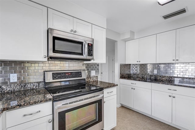 kitchen featuring white cabinets, backsplash, appliances with stainless steel finishes, dark stone counters, and light tile patterned flooring