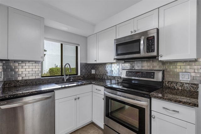 3119 Heatherwood Ln, Sarasota, FL 34235 - kitchen with stainless steel appliances, a sink, white cabinetry, dark stone counters, and decorative backsplash
