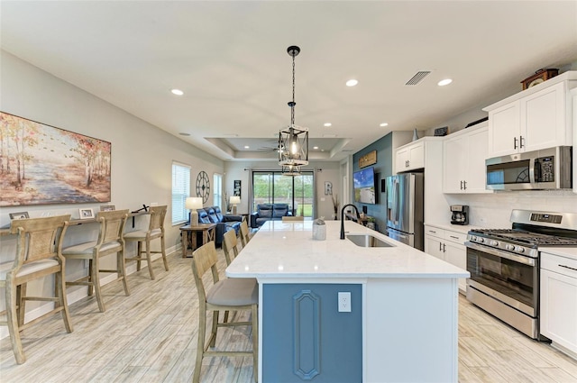 kitchen with appliances with stainless steel finishes, decorative light fixtures, a center island with sink, and light hardwood / wood-style flooring