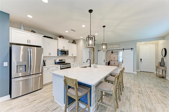 kitchen featuring stainless steel appliances, a center island with sink, hanging light fixtures, a barn door, and sink