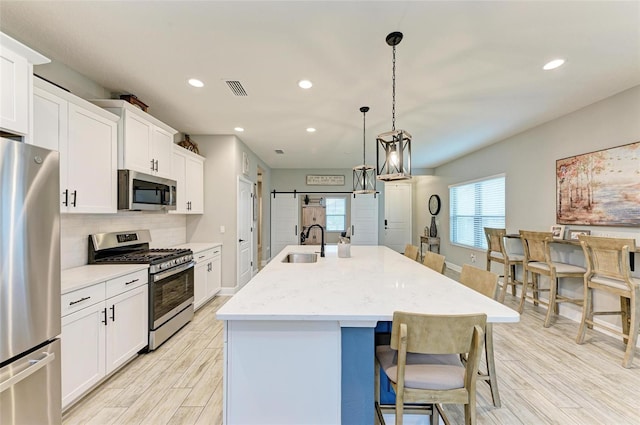 kitchen with stainless steel appliances, light wood-type flooring, a barn door, pendant lighting, and an island with sink