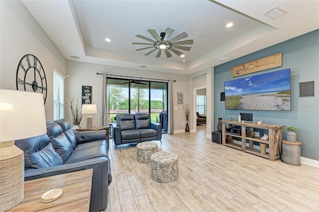 living room featuring ceiling fan, light hardwood / wood-style flooring, and a tray ceiling