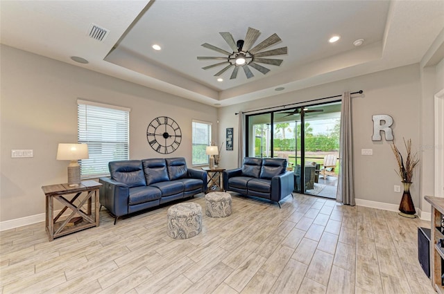 living room featuring ceiling fan, light wood-type flooring, and a tray ceiling