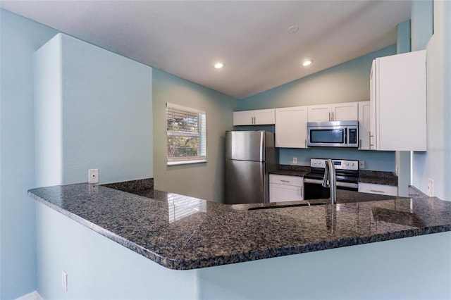 kitchen with kitchen peninsula, vaulted ceiling, appliances with stainless steel finishes, white cabinets, and dark stone counters