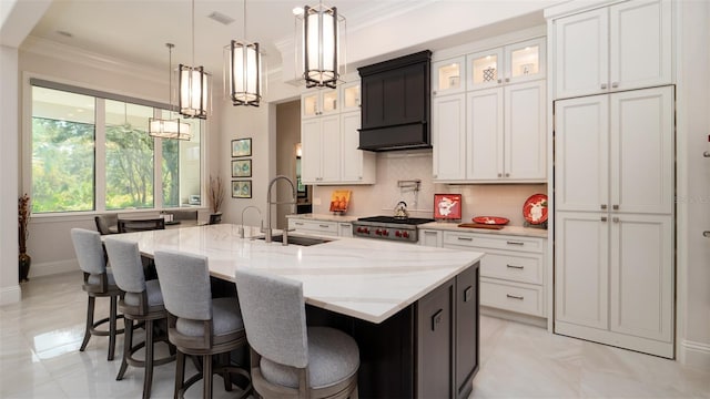 kitchen featuring pendant lighting, sink, a kitchen island with sink, light stone countertops, and white cabinetry