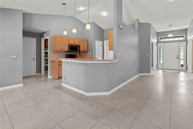 kitchen with high vaulted ceiling, kitchen peninsula, decorative light fixtures, and light tile patterned flooring