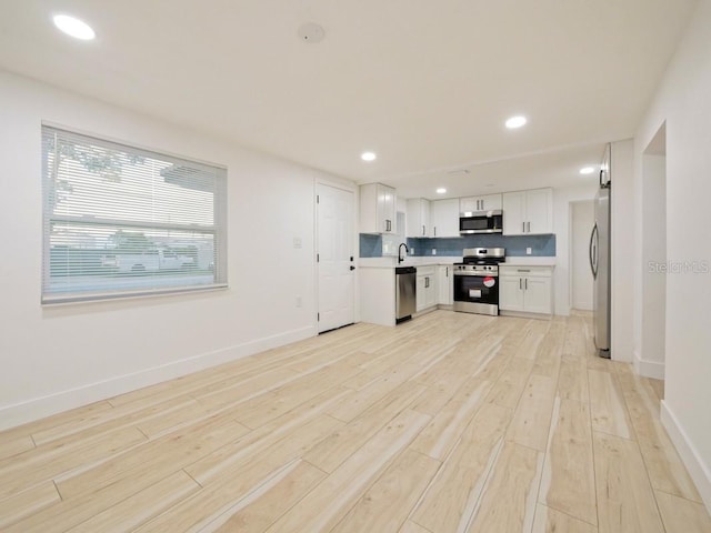 kitchen with stainless steel appliances, decorative backsplash, light wood-type flooring, and white cabinets