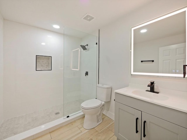 bathroom with toilet, hardwood / wood-style floors, vanity, and a tile shower