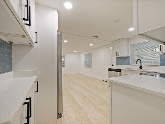 kitchen featuring white cabinets, tasteful backsplash, stainless steel dishwasher, light wood-type flooring, and light stone counters