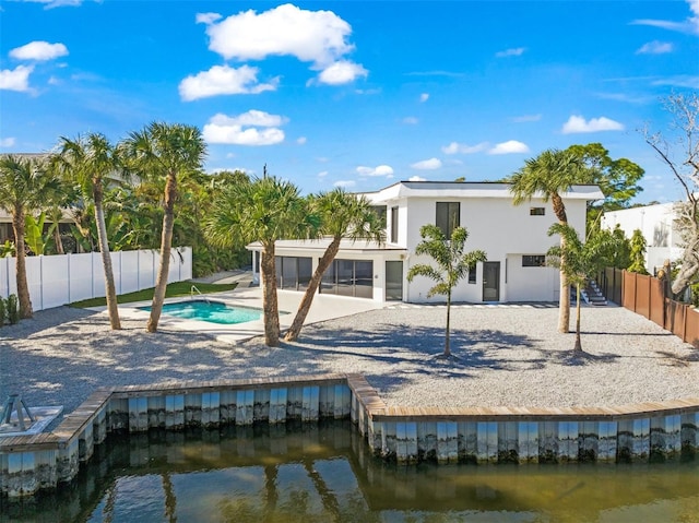 rear view of property featuring a water view, a patio area, and a fenced in pool