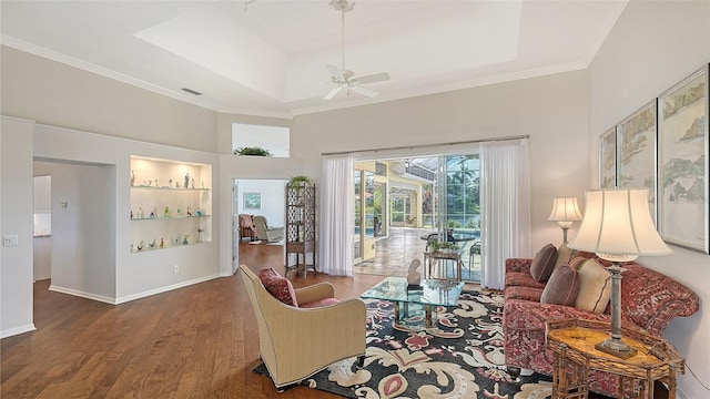 living room featuring ceiling fan, a towering ceiling, a raised ceiling, crown molding, and dark wood-type flooring