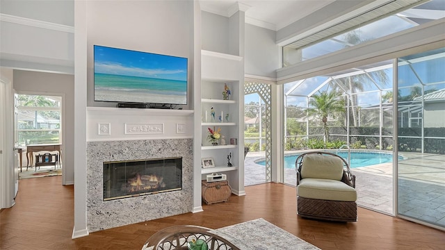 living room with built in shelves, crown molding, a fireplace, hardwood / wood-style flooring, and a high ceiling