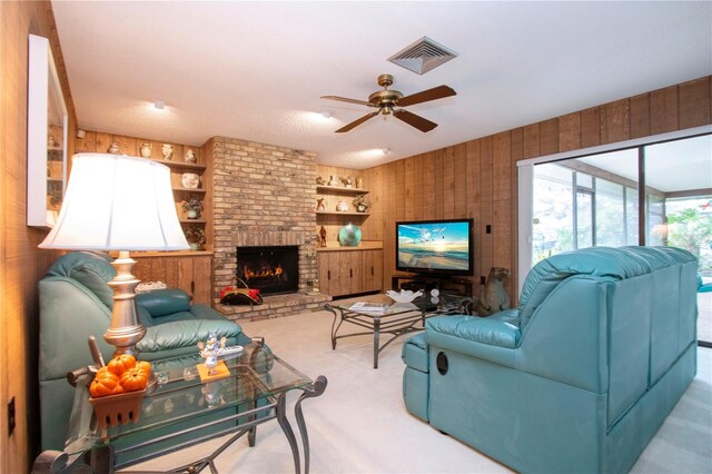 living room featuring wooden walls, light colored carpet, ceiling fan, and a brick fireplace