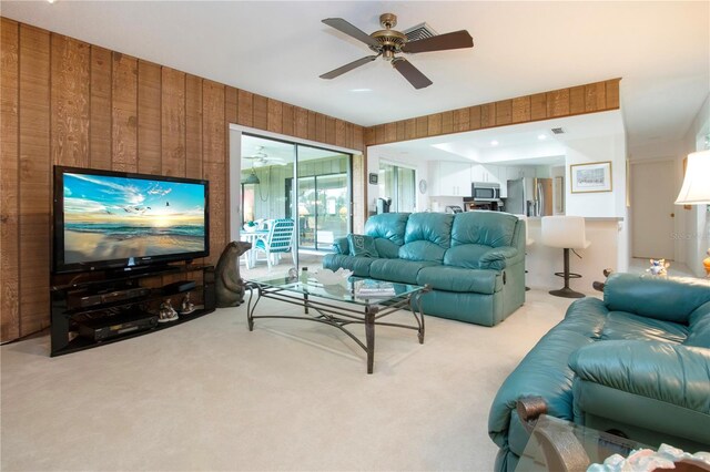 living room featuring wood walls, ceiling fan, and light carpet