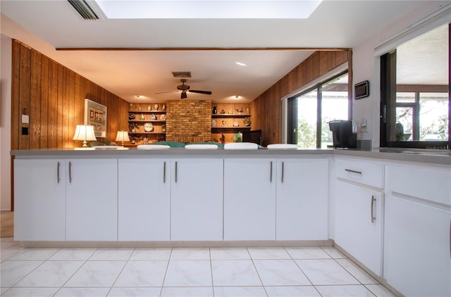 kitchen featuring wood walls, light tile patterned floors, ceiling fan, and white cabinets