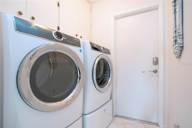 clothes washing area with cabinets, washing machine and dryer, and light tile patterned floors