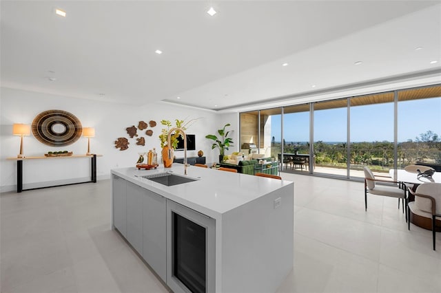 kitchen with white cabinets, a wall of windows, an island with sink, and wine cooler