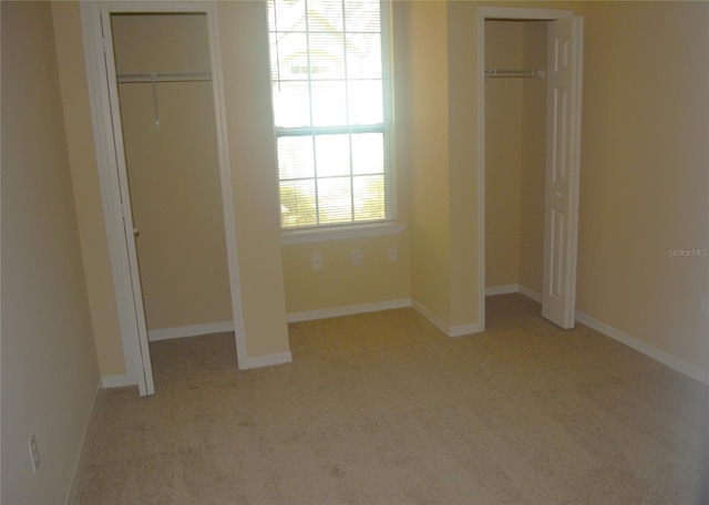 unfurnished bedroom featuring multiple closets and light carpet