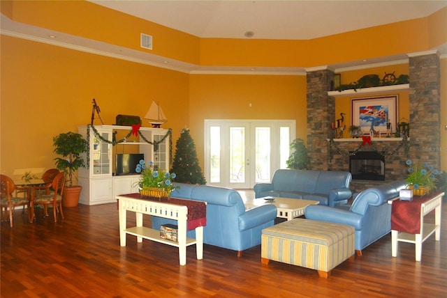 living room with a stone fireplace, wood-type flooring, crown molding, and a towering ceiling