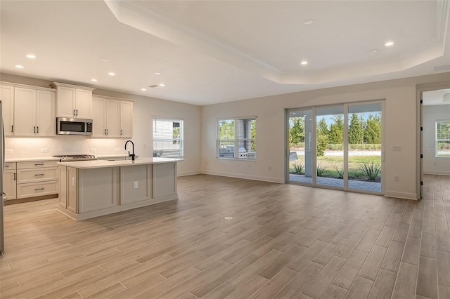 kitchen featuring white cabinetry, sink, a tray ceiling, a center island with sink, and light wood-type flooring