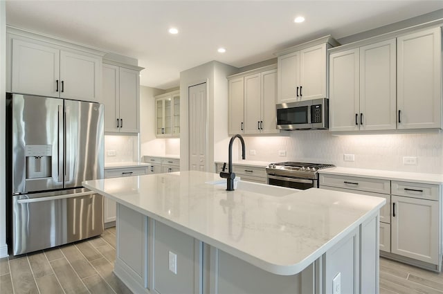 kitchen featuring sink, light stone counters, stainless steel appliances, and an island with sink