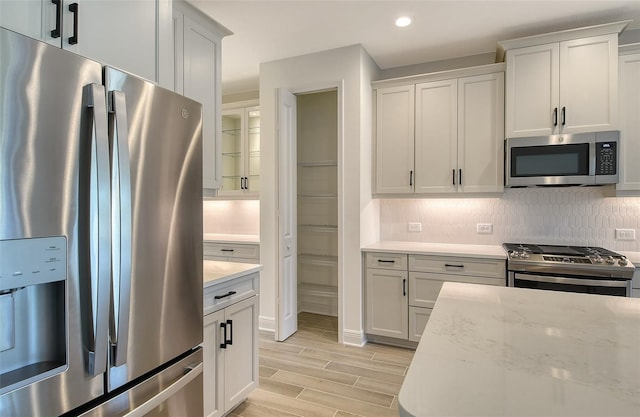 kitchen featuring white cabinets, appliances with stainless steel finishes, light hardwood / wood-style flooring, and light stone counters