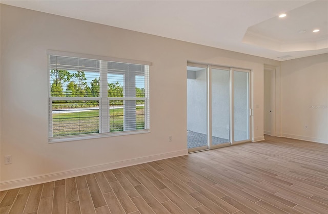 unfurnished room with light wood-type flooring, a tray ceiling, and plenty of natural light