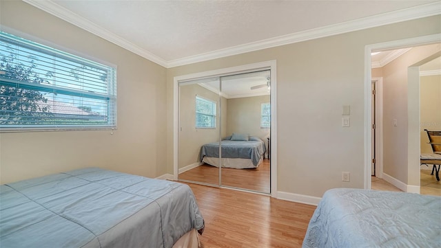 bedroom with light wood-type flooring, crown molding, and a closet