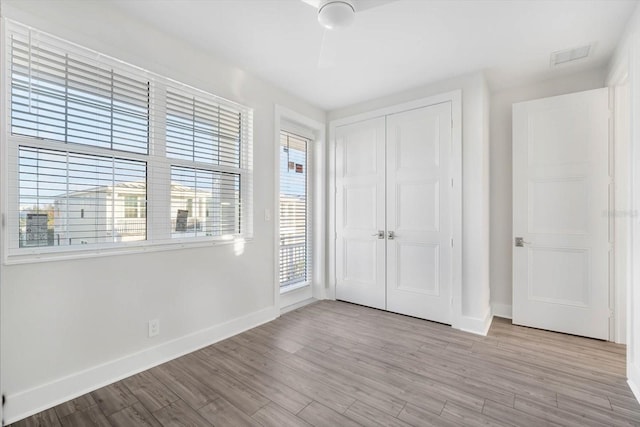 unfurnished bedroom with multiple windows, ceiling fan, a closet, and light wood-type flooring