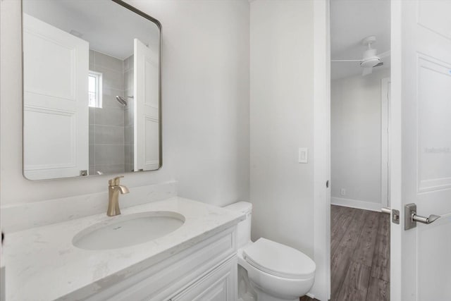 bathroom with a tile shower, vanity, ceiling fan, hardwood / wood-style floors, and toilet