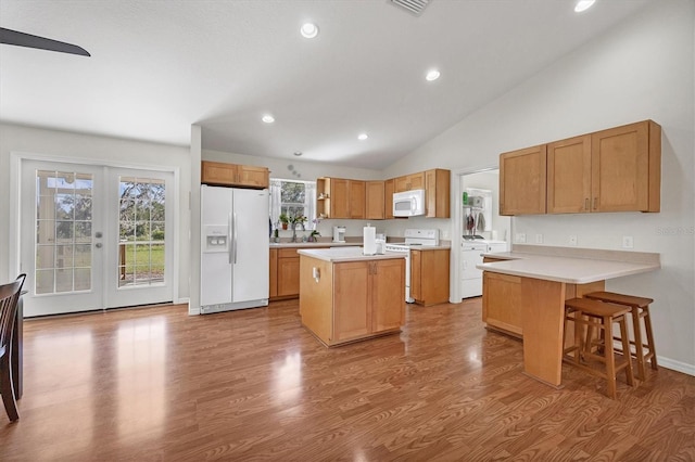 kitchen with lofted ceiling, recessed lighting, white appliances, wood finished floors, and light countertops